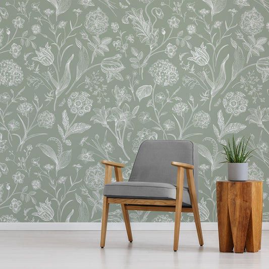 A living room with a grey chair and amber coloured side table showing 'Priscilla' which is a botanical wallpaper featuring delicate white floral and plant illustrations on a soft green background in a vintage-inspired repeating pattern.