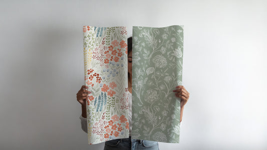 A Woman Holding Up Two Different Wallpapers From Peel & Paper