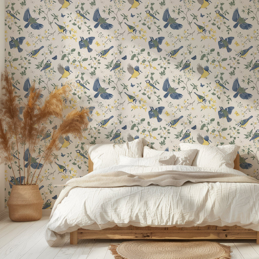 A bedroom with a palette framed bed with white bedding and pampas grass next to it featuring 'Adriana' which is a vintage wallpaper featuring colourful birds, butterflies, blooming flowers and leafy branches in an elegant Chinoiserie-inspired repeating botanical pattern.