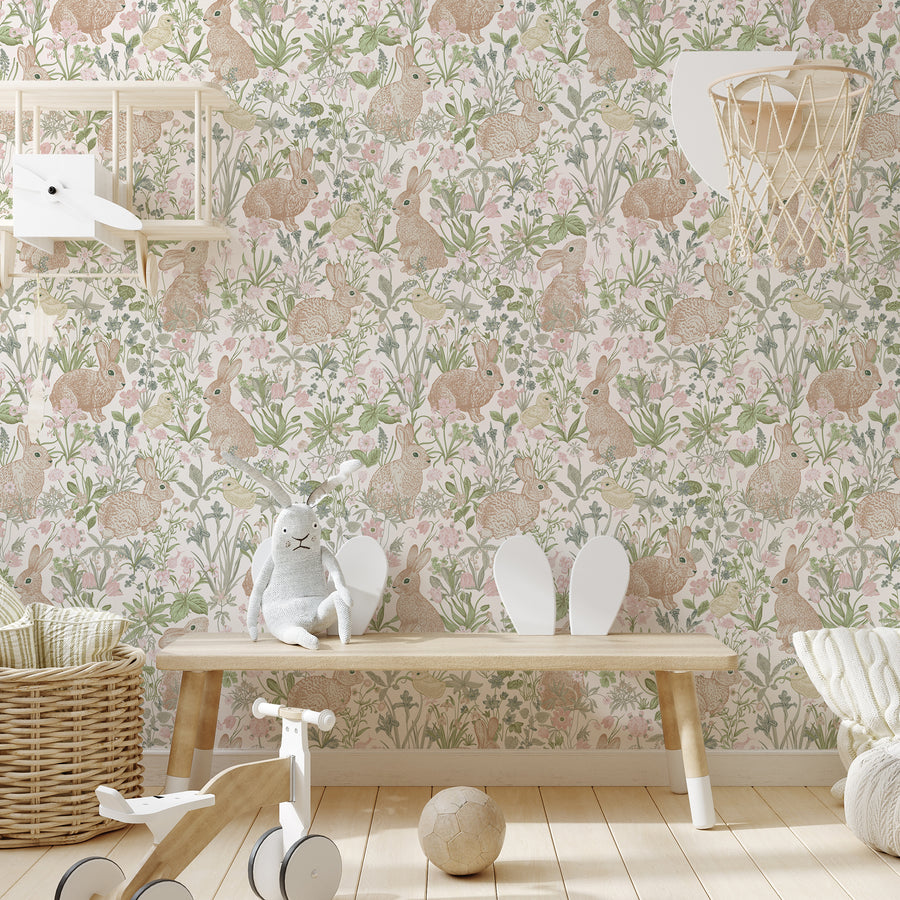 A children's nursery with light coloured furniture featuring the April wallpaper which has hand-drawn rabbits, fluffy chicks, flowers and leafy plants in soft pastel colours on a light background with a repeating pattern.