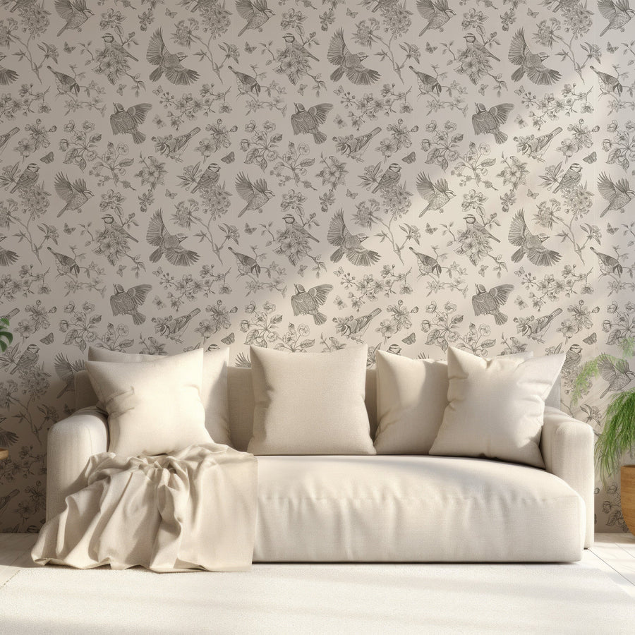 A living room with a cream coloured sofa with the Gianna wallpaper which is beige coloured featuring vintage-style birds, butterflies, flowers and leafy branches in an elegant repeating botanical pattern.