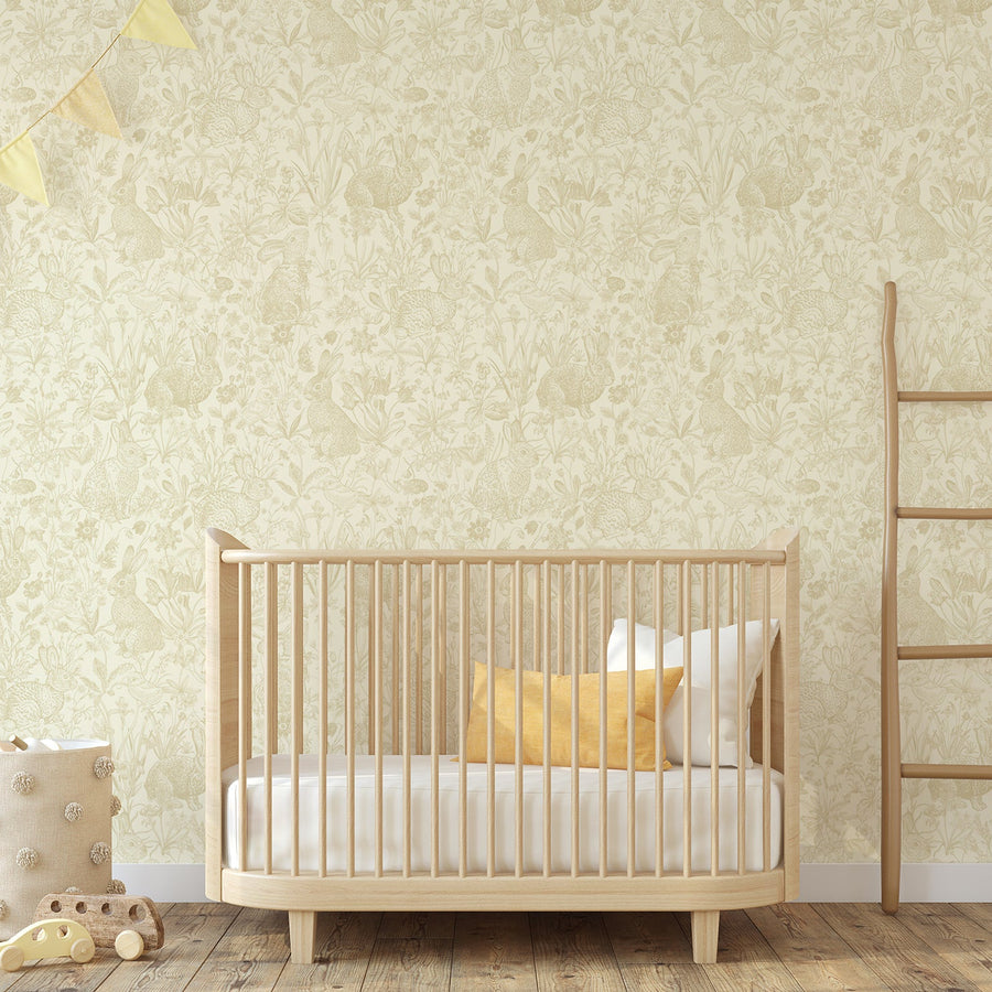 A children's nursery with light coloured furniture featuring the Pascha wallpaper which has yellow rabbits, fluffy chicks, wildflowers and leafy plants in a hand-drawn repeating pattern on a light background.