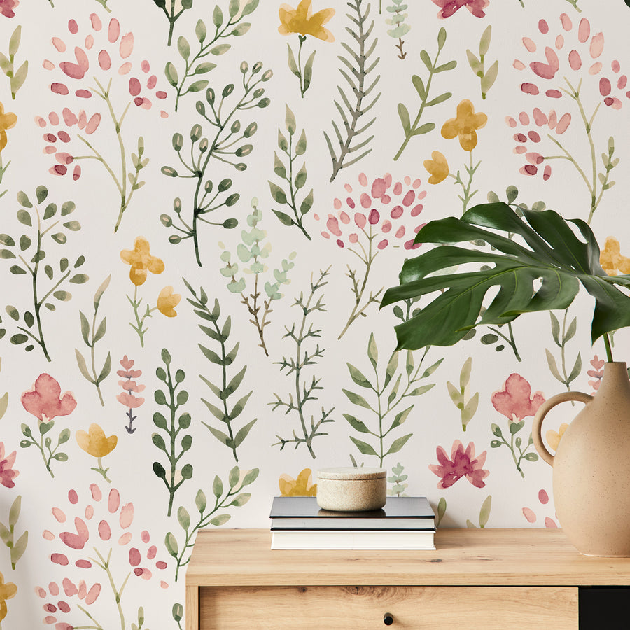 A living room with a side cupboard showing 'Rosanna' which is a watercolour wallpaper featuring delicate flowers and leafy plants in soft green, yellow and pink tones on a beige background in a vibrant repeating botanical pattern.
