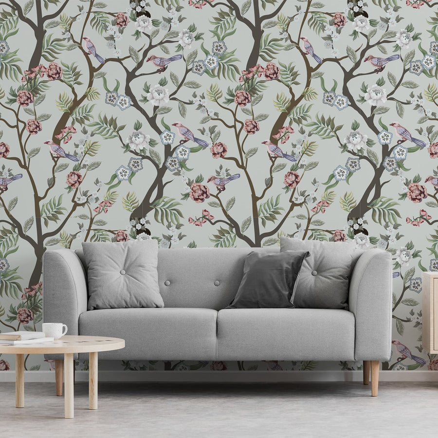 A living room with a grey sofa featuring the Ava wallpaper which is a chinoiserie style with decorative birds, flowering branches and vibrant peonies arranged in a repeating pattern.
