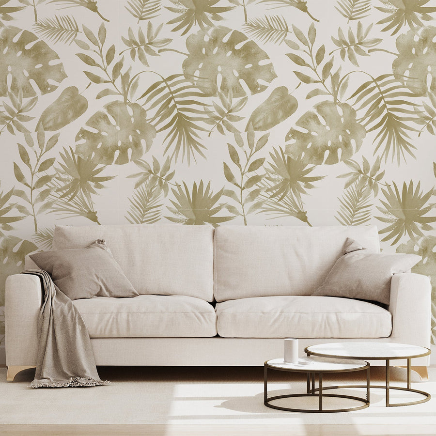 A living room with a two seater cream sofa and marble coffee table featuring 'Lilliana' which is a tropical wallpaper featuring golden watercolour palm leaves and botanical foliage on a soft cream background in an elegant repeating pattern.
