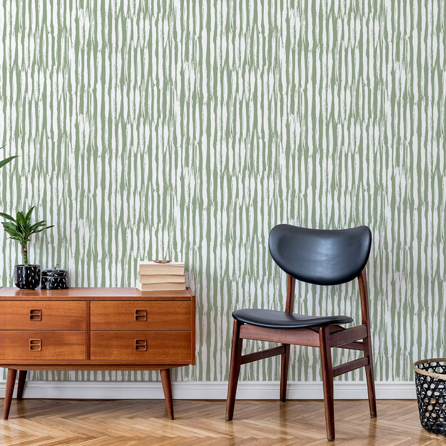 A living room with a black leather chair next to an amber side cupboard showing 'Piper' which is a green and white wallpaper featuring thin vertical lines in a simple striped pattern with a clean, modern geometric design.