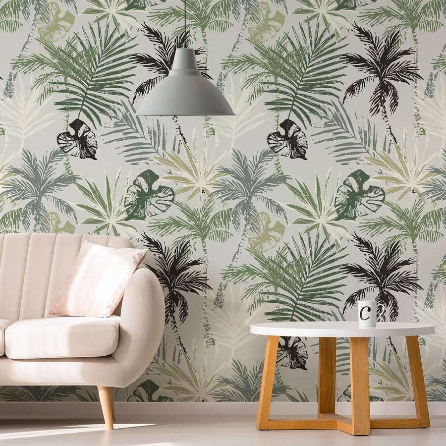 A living room with a light pink sofa, hanging light and white coffee table featuring 'Reagon' which is a abstract tropical wallpaper featuring stylised palm trees and leafy foliage in shades of green on a cool grey background in a modern repeating botanical pattern.